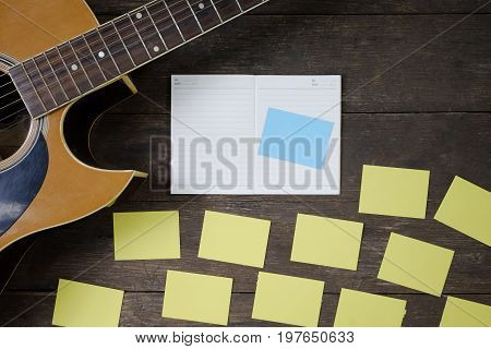 Desk of song composer for a work songwriter with a guitar and notepad on wood table with vintage tone.
