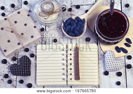 Open notebook with copy space, jars with jam and sugar, spoon with fresh berry, top view. Making fruit jam concept. Fresh berry on wooden table, summer still life and rustic food vintage background