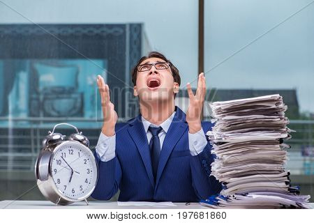 Businessman with pile stack of paper paperwork and an alarm cloc