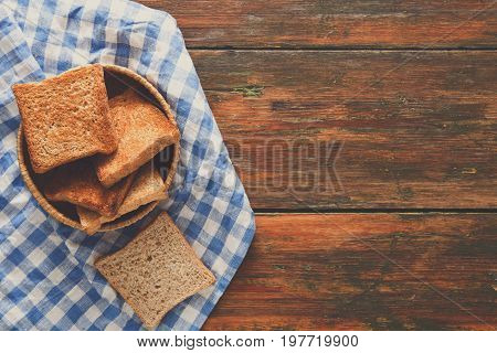 Breakfast background, white bread toasts in wicker breadbasket on checkered table napkin half covering wooden table, top view, copy space