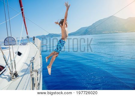Boy jump in sea of sailing yacht on summer cruise. Travel adventure, yachting with child on family vacation.