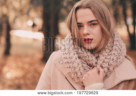 portrait of young beautiful woman walking in stylish warm outfit in sunny autumn day in park wearing pink coat and knitted snood. Casual lifestyle in the city