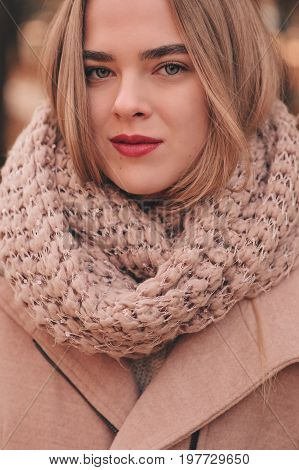 portrait of young beautiful woman walking in stylish warm outfit in sunny autumn day in park wearing pink coat and knitted snood. Casual lifestyle in the city