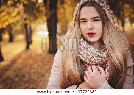 portrait of young beautiful woman walking in stylish warm outfit in sunny autumn day in park wearing pink coat and knitted snood. Casual lifestyle in the city