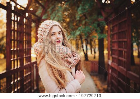 portrait of young beautiful woman walking in stylish warm outfit in sunny autumn day in park wearing pink coat and knitted snood. Casual lifestyle in the city