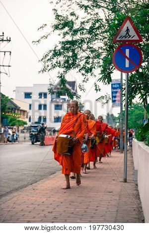 LUANG PRABANG LAOS - MARCH 12 2017: Vertical picture of many monks going in line to Buddhist Alms Giving Ceremony where local people offers food and money before the sunrise in Luang Prabang Laos.