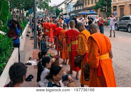 LUANG PRABANG LAOS - MARCH 12 2017: Horizontal picture of local people giving food and money to the monks for the Buddhist Alms Giving Ceremony in Luang Prabang Laos.