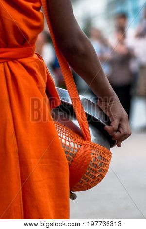 Hand of young monk carrying a basket to collect food and money for the Buddhist Alms Giving Ceremony in Luang Prabang Laos.