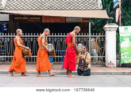 LUANG PRABANG LAOS - MARCH 12 2017: Lao woman on her knees giving to the monks food and money for the Buddhist Alms Giving Ceremony before the sunrise in Luang Prabang Laos.
