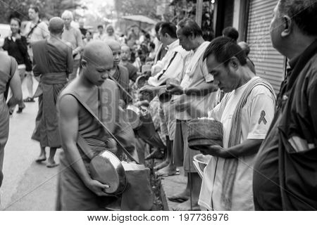 LUANG PRABANG LAOS - MARCH 12 2017: Black and white picture with movement of local people giving food and money to the monks for the Buddhist Alms Giving Ceremony in Luang Prabang Laos.