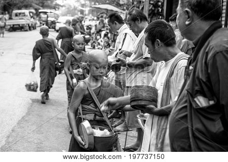 LUANG PRABANG LAOS - MARCH 12 2017: Black and white picture of local people giving food and money to the monks for the Buddhist Alms Giving Ceremony in Luang Prabang Laos.