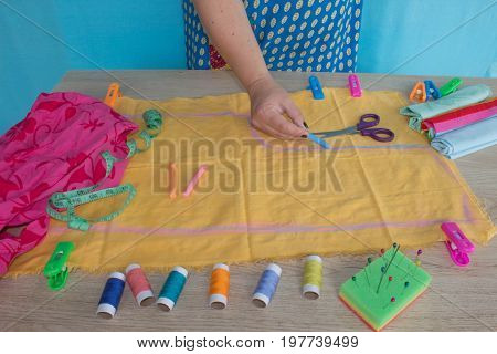 Close up of woman's hands drawing a pattern on yellow tissue. Measuring tape and sewing accessories. A tailor is laying out a dress/Sewing layout