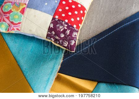 quilting, patchwork, sewing, tailoring and fashion concept - close-up beautiful stitched cushion, macro on pillow with background of blue, gray and sand stitched scraps of fabric, flat lay, top view