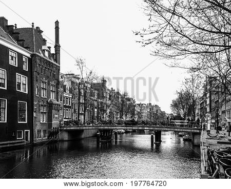 Water canal, aka gracht, and narrow houses along it in Amsterdam city centre, Netherlands, black and white image.