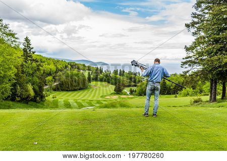 Landscape view of green golf course with hills in summer in La Malbaie Quebec Canada in Charlevoix region with photographer and tripod