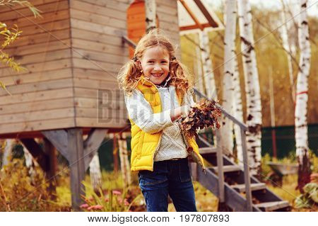 happy child girl playing little gardener in autumn and picking leaves into basket. Seasonal garden work. Backyard cleaning.