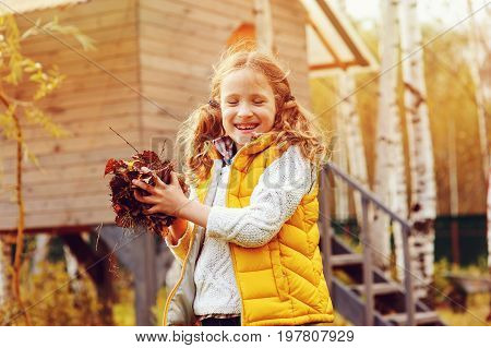 happy child girl playing little gardener in autumn and picking leaves into basket. Seasonal garden work. Backyard cleaning.