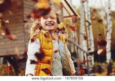 happy child girl playing little gardener in autumn and picking leaves into basket. Seasonal garden work.