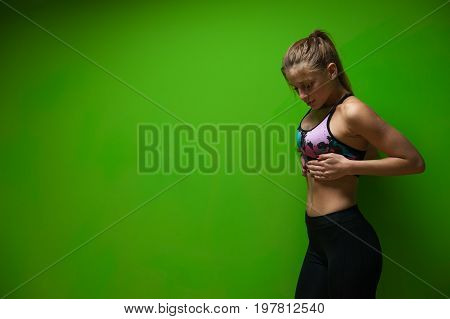 Fit young woman wearing sportswear posing over green background and showing abdominal. Healthy lifestyle and fitness concept.