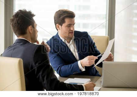 Two serious business partners discussing financial report, analyzing teamwork results, businessman pointing at document, negotiating about contract terms, senior manager giving instructions to junior