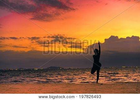 Young woman yoga exersice posting silhouette on the beach in summer
