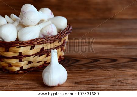Raw garlic bulbs in a basket on a wooden background with empty place for text. Harvesting garlic concept. Young garlic background