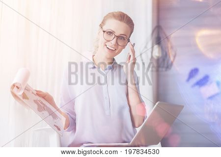 Busy day. Joyful beautiful smiling woman yalking on cell phone and using laptop while working as a freelancer at home