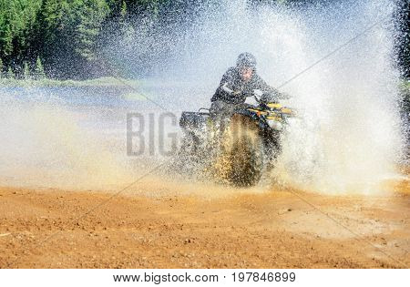 Man driving ATV quad through splashing water with high speed on a beach.