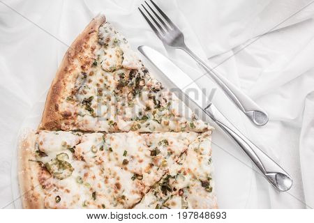Pieces of pizza on a plate fork and knife on a white tablecloth