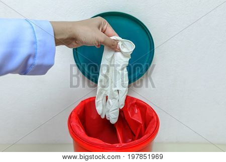 Closeup cropped portrait healthcare professional throwing away blue disposable latex gloves in trash.lsolated lab background.infectious wastes in red bag in hospital.