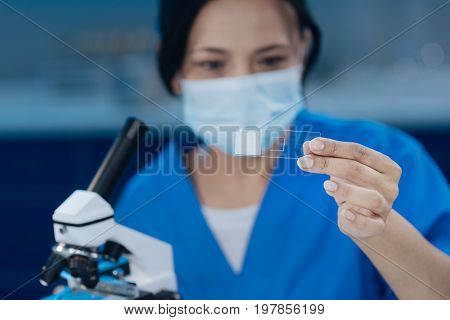 Test sample. Selective focus of a microscope slide being held by a smart professional nice researcher while studying it