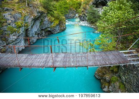 small rope bridge over green Utla river in Utladalen, Norway