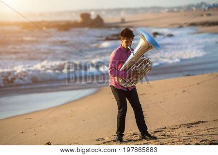 Young man play Tuba musical instrument on sea shore outdoor.