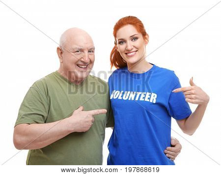 Young woman and senior man pointing at t-shirt with text VOLUNTEER, on white background