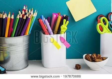 School background: a white brick wall with accessories, pencils, tetrads, scissors, an apple, pecans, a board for a substitute placed in front of her on the table. Selective focus