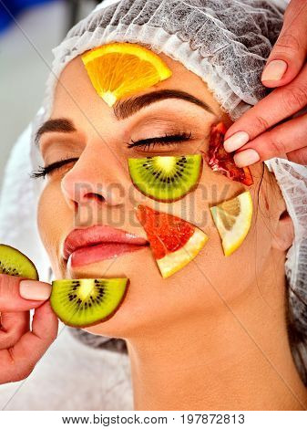 Facial mask from fresh fruits for woman. Beautician apply slices of avocado, grapefruit and kiwi. Girl in medical hat lying on spa bed for skin care procedure in salon. Mask against sagging skin.