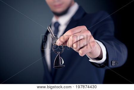 Young businessman hand over keys with empty dark background