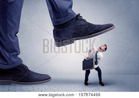 Young handsome businessman getting crushed by a big formal shoe