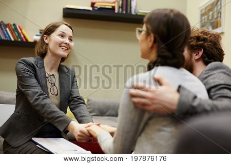 Portrait of smiling female psychiatrist holding clients hands heartily congratulating on progress in couples counseling