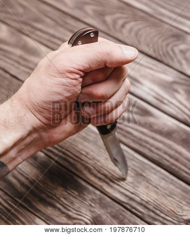 Man holding stainless jackknife on a wooden background view of hand.
