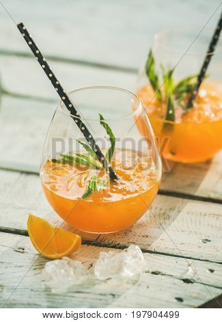Refreshing cold alcoholic summer citrus cocktail with orange, peppermint and ice in stemless glasses over light blue wooden table background, selective focus