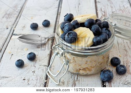 Overnight oats with fresh blueberries and bananas in a jar on a rustic white wood background