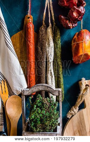 Assortment of traditional Spanish charcuterie meat sausages fresh herbs thyme kitchen utensils towel wood cutting board rustic interior
