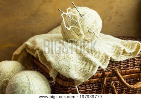 Handmade knitwear clew of white wool yarn on vintage hobby and crafts wicker chest wool clews wood table cozy atmosphere shabby chic style