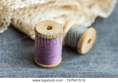 Vintage wood spools with lilac and grey threads on folded wool fabric cotton off-white lace hobby swing concept copyspace header for website