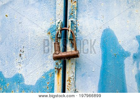 Rusty padlock hanging on a blue metallic background