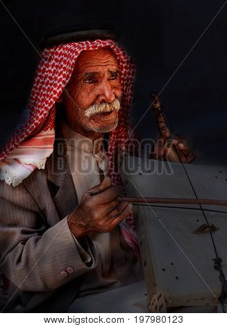 Little Petra Jordan - June 20 2017: Old Bedouin man or Arab man in traditional outfit playing his musical instrument at the doorway of Little Petra.