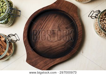 There Are Empty Round Wooden Tray, Cordamom, Cinnamon Bark, Nuts And Pepercorns In Glass Jars.