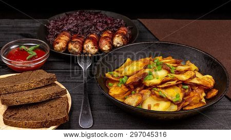 Roasted Potato In The Pot, Pieces Of Rye Black Bread On A Wooden Serving Plate, Homemade Sausages In