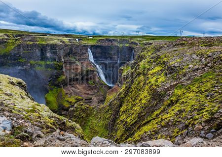  High waterfall Hayfoss in a picturesque and dangerous tundra canyon. The concept of extreme and phototourism. Cloudy and windy summer day in Iceland